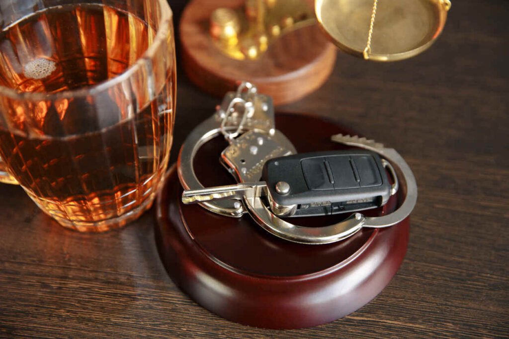 A car key fob, handcuffs, and a glass of alcohol on a table with scales of justice in the background, symbolizing the legal consequences of DUI accidents in St. Louis.